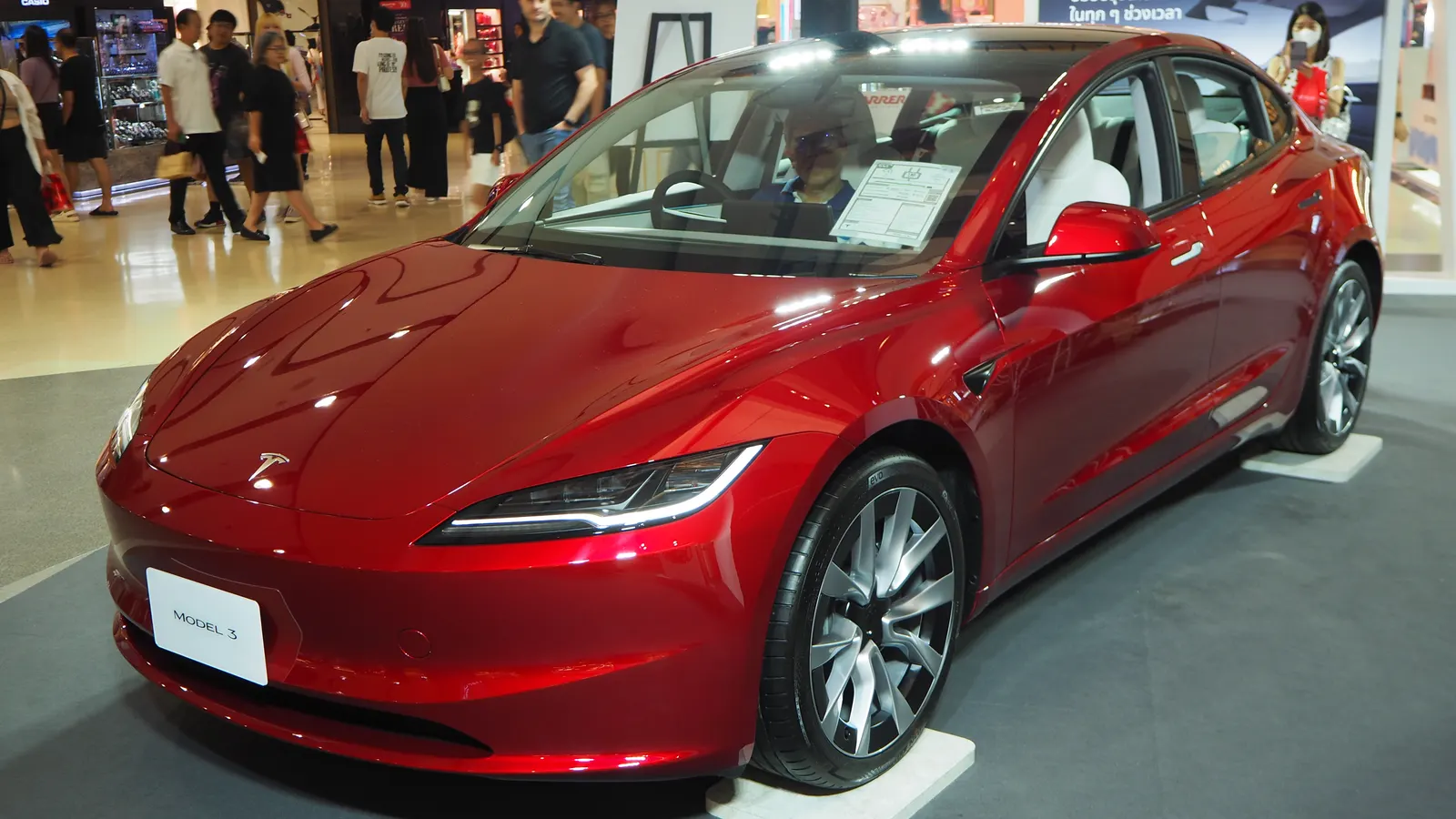 Red Tesla Model 3 sedan, current generation, front three-quarter view at an indoor display