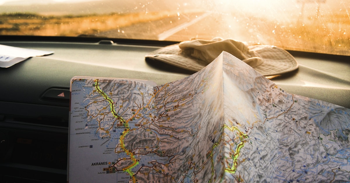 A driver's hand on a map on the dashboard, planning a driving route