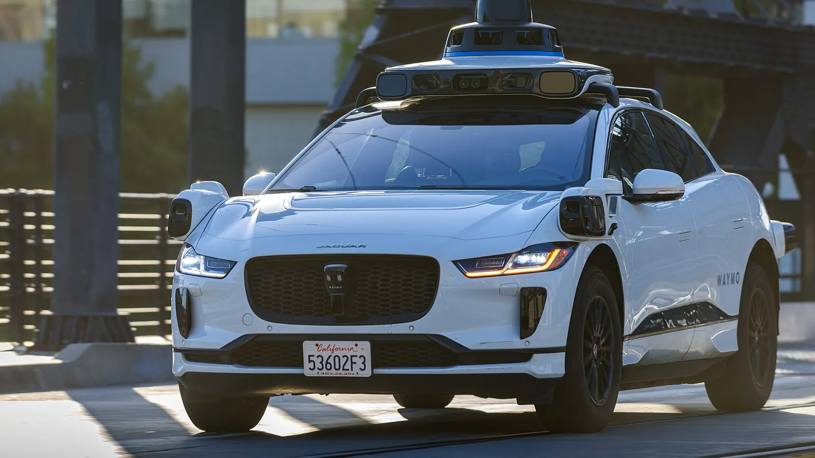 Waymo Jaguar I-Pace robotaxi with roof-mounted sensors, front three-quarter view, on a California street