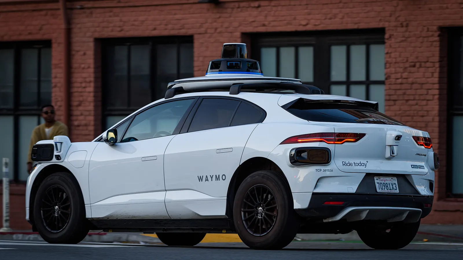 Waymo Jaguar I-Pace robotaxi, rear three-quarter view, parked by a brick building in California