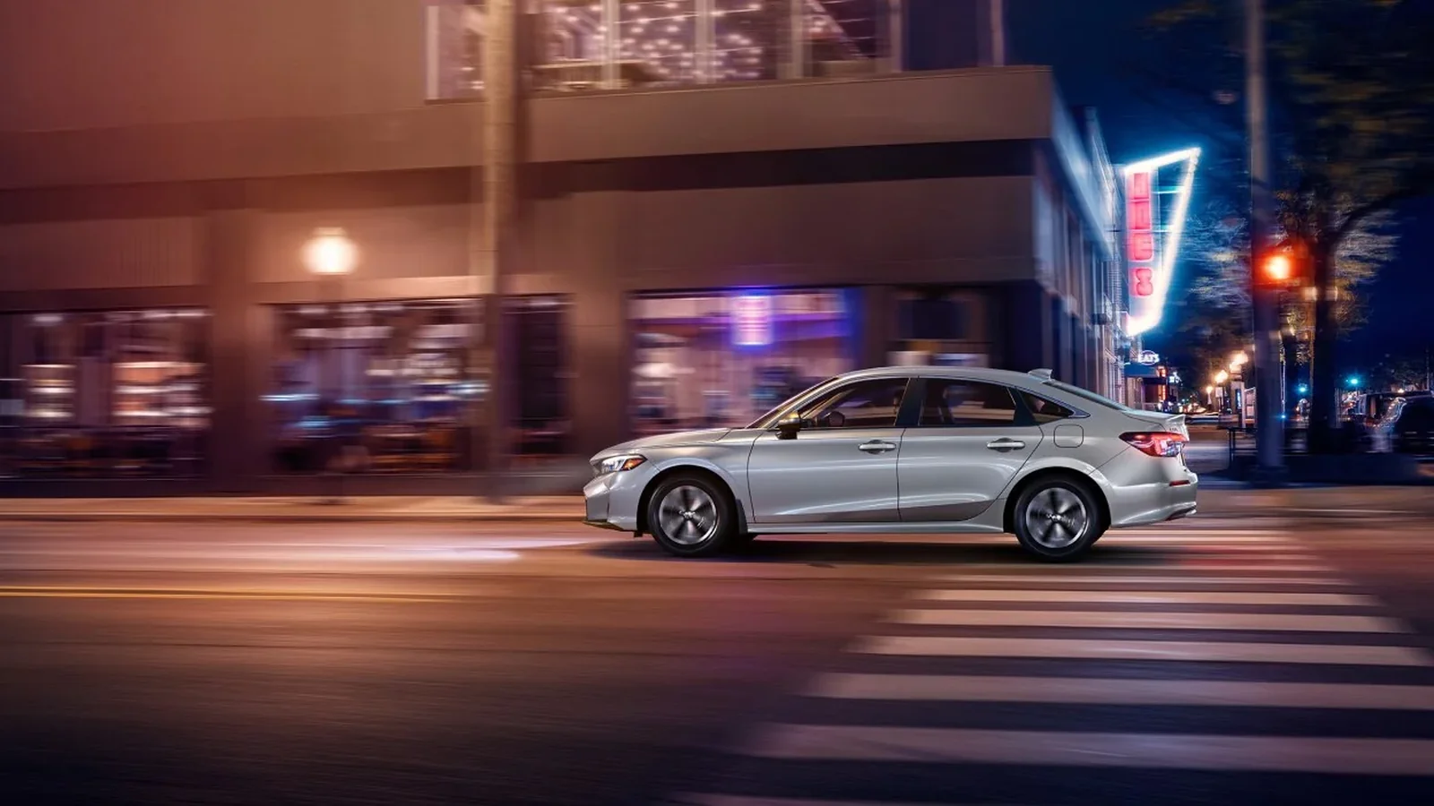 2026 Honda Civic Sedan in silver driving on a city street at night, Canadian model
